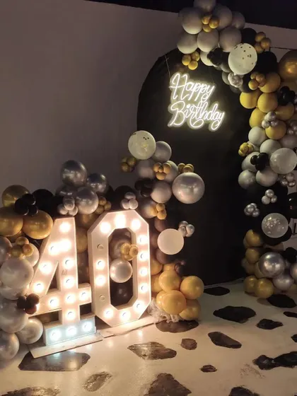 Celebrating the big 4-0 with a sophisticated black, gold, and silver theme. This setup includes a balloon arch against a black backdrop, a neon sign, and large marquee numbers.