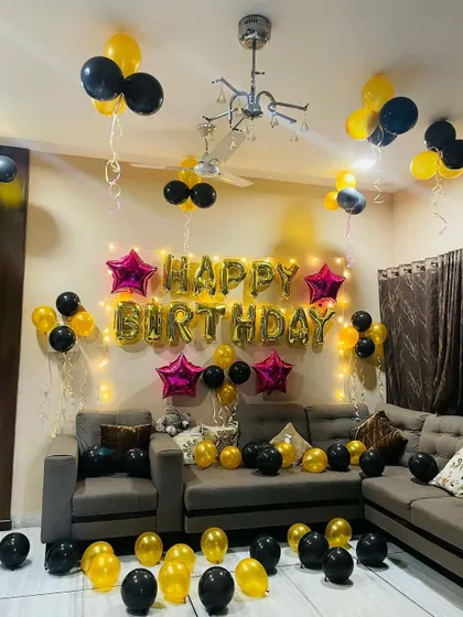 A living room birthday decoration with black and yellow balloons and star-shaped foil balloons.