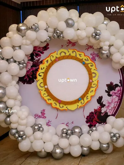 A circular photo booth backdrop framed with white and silver balloon's.