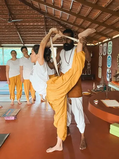 With the help of a strap, I assist a student in an advanced standing split variation. This demonstrates how we can work towards deeper flexibility with safety and support, honoring the body's current abilities while gently encouraging growth.