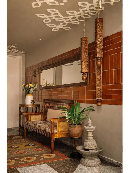 A full view of the private foyer, where suspended carved pillars, a ceiling 'kolam', and earthy prints create a warm and inviting entrance. The space is designed to feel like a modern interpretation of a traditional South Indian home.
