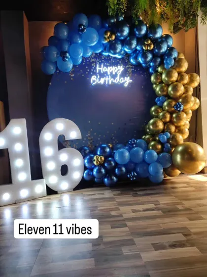 A cool and sophisticated theme for a 16th birthday. The decor features a deep blue backdrop, a balloon arch in shades of blue and gold, a neon sign, and large marquee numbers for the age.