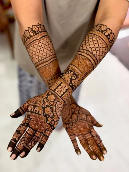 The back of the hands for a baby shower mehendi, featuring "MA" and "PA" initials and dense traditional patterns.