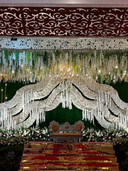 For this modern reception stage, I designed a beautiful arch made of shimmering white crystals over the main seating area. The backdrop is a simple green wall, which makes the crystal arch and the hanging floral arrangements stand out.