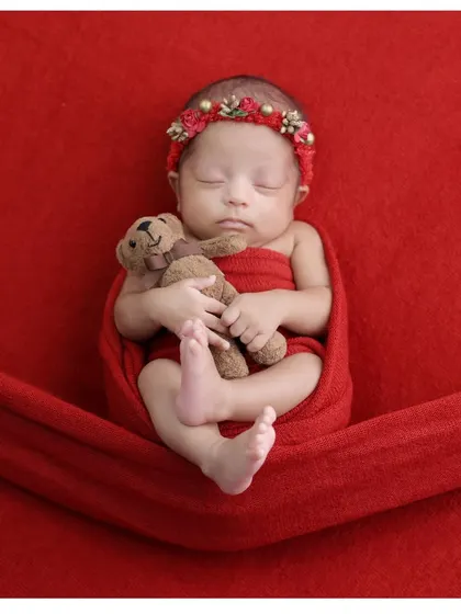 A sweet portrait of a sleeping baby girl in a red wrap, cuddling a tiny teddy bear. The simple setup allows her peaceful expression to be the main focus.