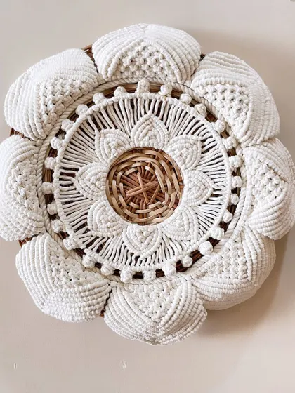 This design combines the natural texture of a wicker basket with the softness of macrame. The intricate white cotton knotting around the woven center creates a stunning, layered floral medallion for your wall.