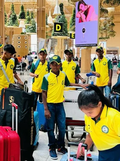 The team navigates the airport with their luggage, ready for their international cricket experience.