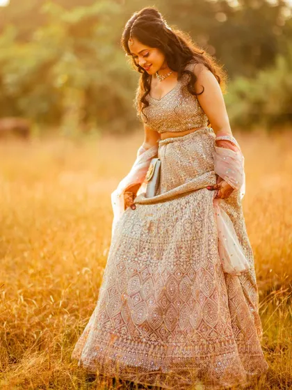 A candid shot of the bride looking down at her lehenga in a sunlit field. This natural, unposed moment captures her elegance and the beauty of her attire.