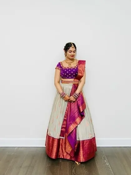The bride stands gracefully in her ivory and purple lehenga, a picture of timeless elegance.