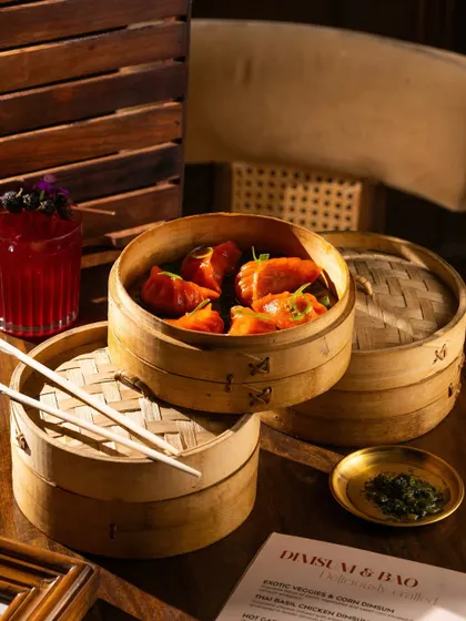 A stack of dim sum steamers in a cozy, warm setting. The lighting emphasizes the textures of the wood and the steam.