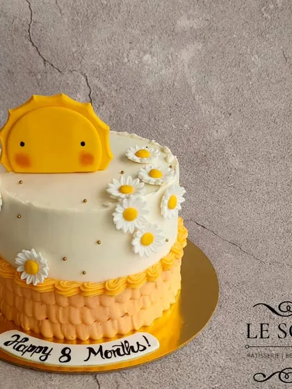 How cute is this sunshine-themed cake for an 8-month celebration? This half-kg Mango Pistachio cake features a cheerful fondant sun, daisy decorations, and a ruffled orange buttercream border.