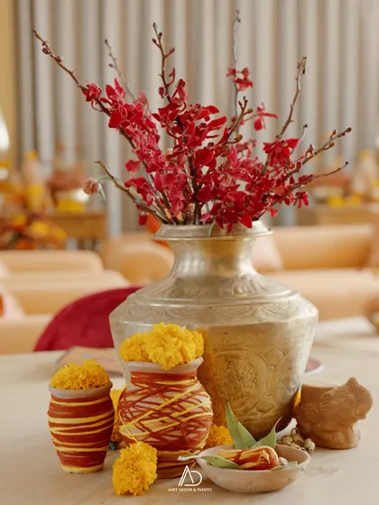 An elegant fusion of traditional elements, with marigolds in small pots, red orchids in a classic silver vase, and other customary items for a Mamera ceremony.