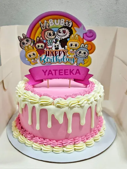 A modern buttercream cake with a pink base, white chocolate drip, and classic piped borders, topped with a cute Labubu character.