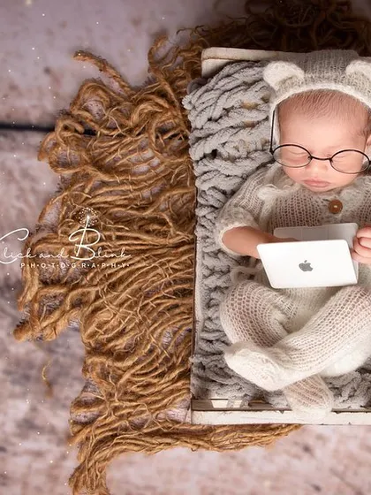 The little scholar. This adorable setup features a baby in a knitted bear outfit and glasses, appearing to work on a tiny laptop. It's a fun and modern take on newborn portraits.