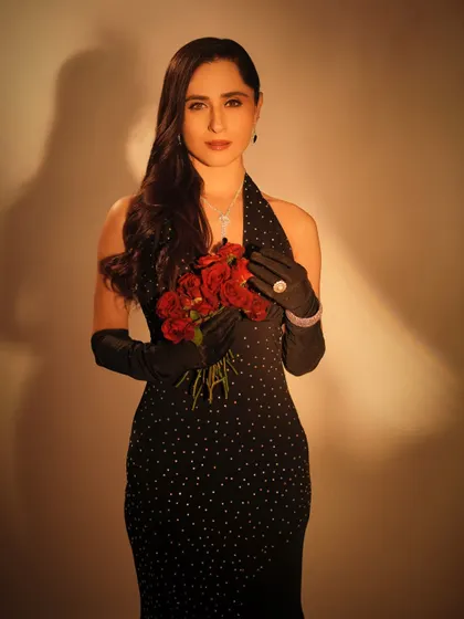 A beautiful medium shot that focuses on the contrast between the dark outfit and the bright red roses. The makeup is kept classic and elegant to match the overall theme.