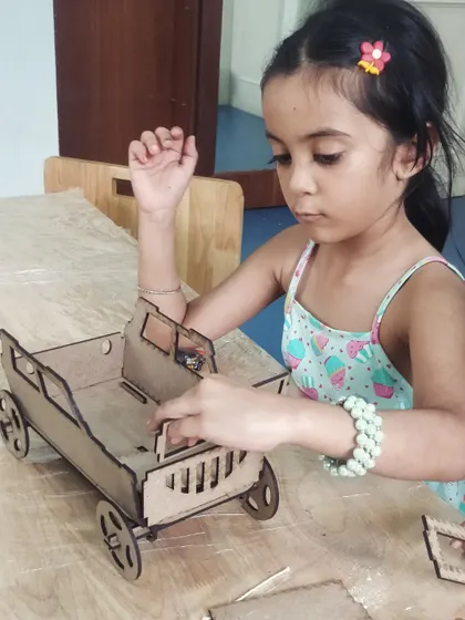 A young girl assembles a vintage-style wooden car model, carefully fitting the pieces together.