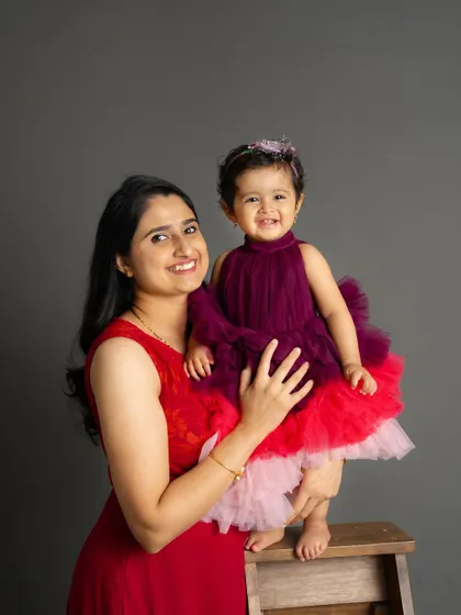 A beautiful mother-daughter portrait filled with smiles. Their coordinating red and purple dresses add a vibrant touch to this classic studio photo.