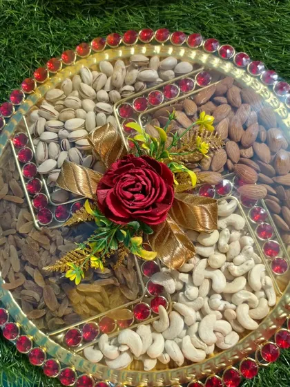 A decorative dry fruit tray prepared for a Roka ceremony. The swastika design made with different nuts and the floral centerpiece make it a perfect auspicious gift.