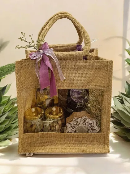 A sustainable and rustic Diwali hamper in a jute bag with a clear window. It's filled with jars of dry fruits and other treats, perfect for eco-conscious gifting.