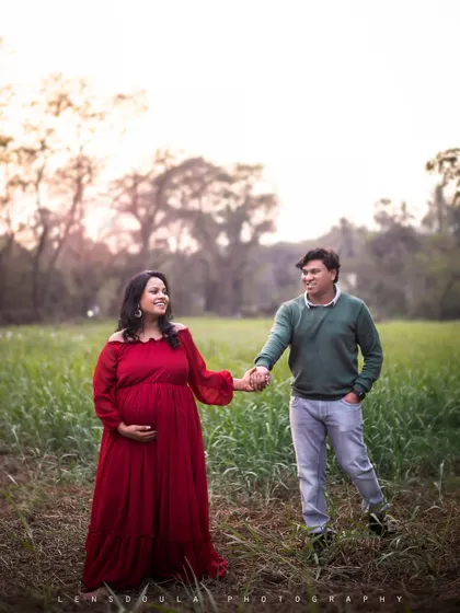 A full-length shot of the couple walking hand-in-hand through a green field. The vibrant red dress stands out beautifully against the natural landscape.
