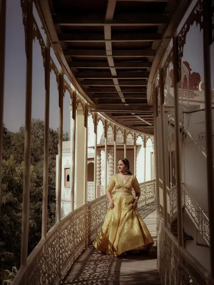 A stunning portrait of the bride in a vibrant yellow lehenga, posing on a balcony with a regal air.