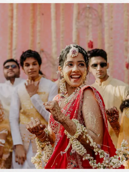 A candid shot of the bride, laughing and dancing, covered in turmeric and flowers, embodying the spirit of the Haldi.