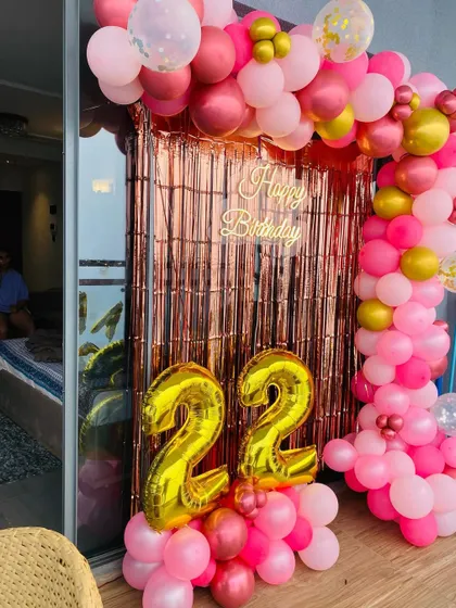 A 22nd birthday decoration on a balcony, featuring a balloon arch in shades of pink and gold over a rose gold foil curtain.