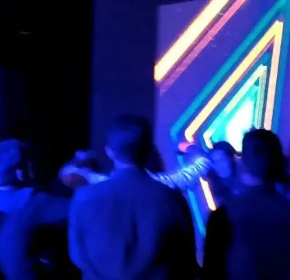 The crowd dances in front of a vibrant, multi-colored LED display.