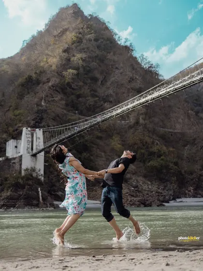 A playful and dynamic shot of a couple splashing in the river, with a suspension bridge creating a dramatic backdrop.