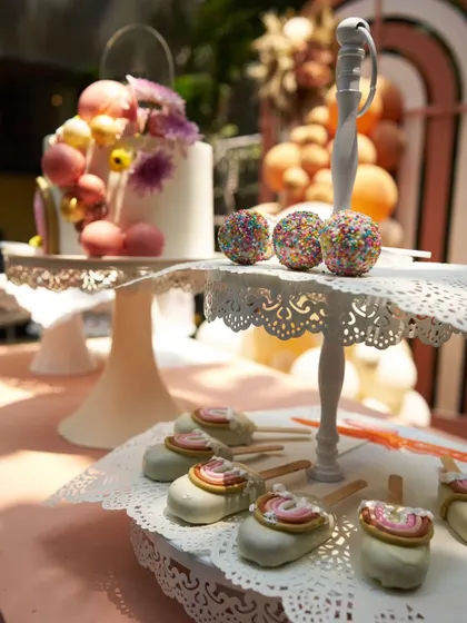 A tiered dessert stand with a variety of sweet treats, including cake pops and a beautifully decorated cake, all sticking to the warm, boho color palette.