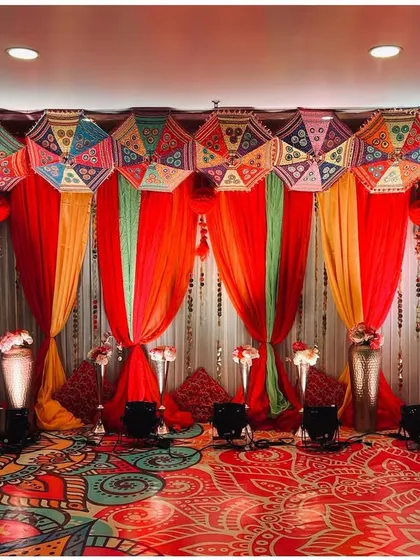 A vibrant Mehendi stage with colorful drapes, Rajasthani umbrellas, and a patterned floor.