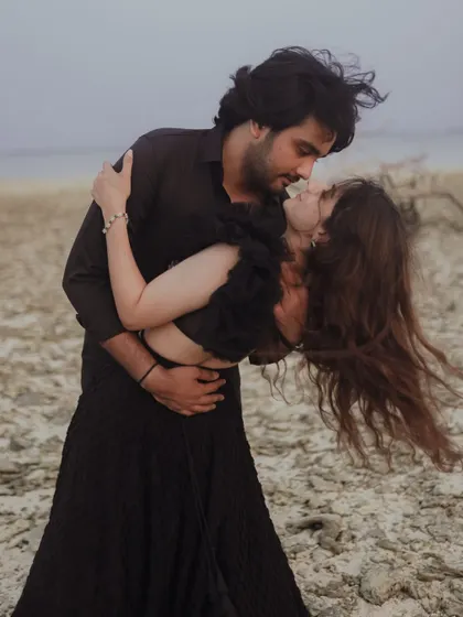 A passionate dip against the dramatic, windswept backdrop of a secluded beach. This image captures raw emotion and movement, telling a story of intense love.