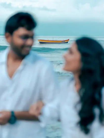 An artistic shot focusing on the boat in the distance, with the couple softly blurred. This creative composition adds depth and a sense of story to a beach pre-wedding session.