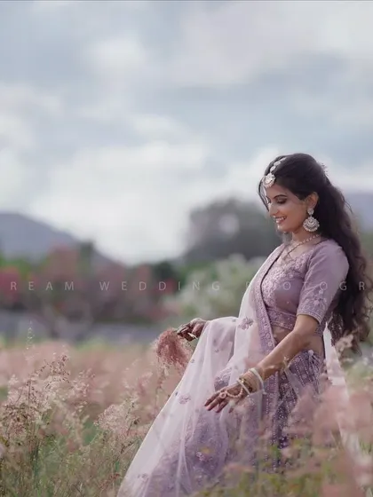 A candid shot of the bride in a field of flowers. The soft purple tones in her makeup subtly pick up the color of her lehenga.