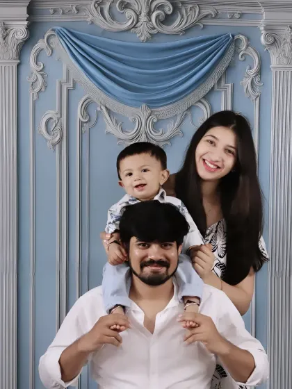 A playful family photo with the smiling baby enjoying a shoulder ride from his dad, with mom looking on happily.