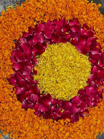 A beautiful rangoli made from fresh flower petals, using orange and yellow marigolds with red rose petals for a colorful and natural floor decoration.