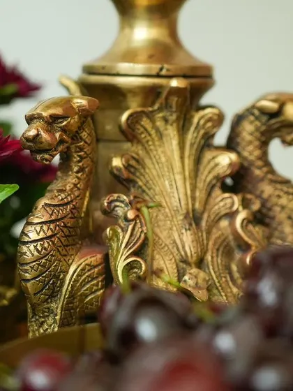 A close-up of an antique brass prop with intricate dragon carvings, surrounded by deep red flowers and fresh cherries.