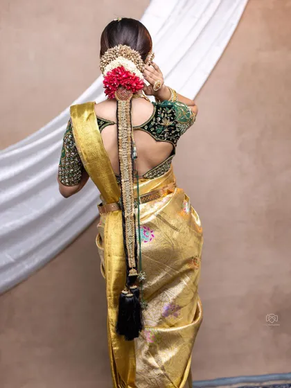A back view of a bridal blouse made from rich velvet. The sleeves are heavily embroidered, complementing the golden Kanjeevaram saree perfectly for a luxurious Muhurtham look.