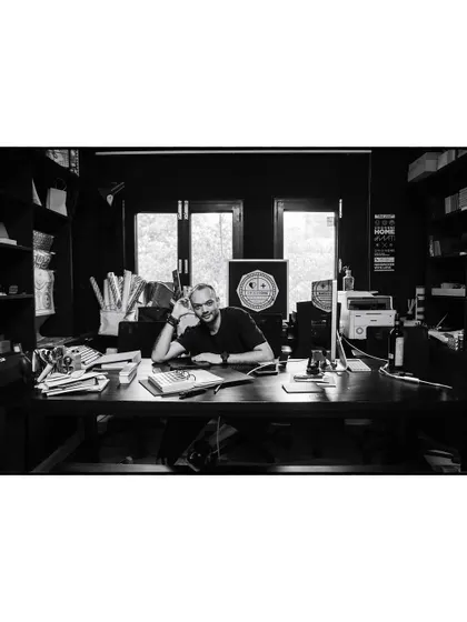 A wide shot of artist Pushkar Thakur in his studio, surrounded by his work. This black and white environmental portrait tells the story of his creative world.