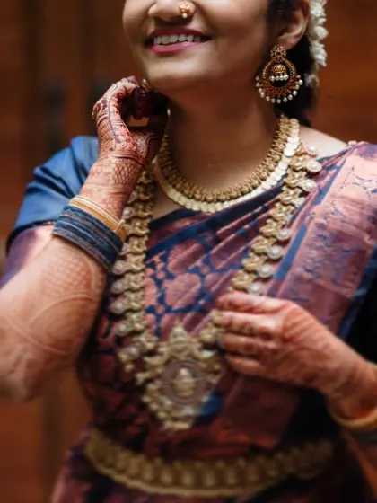 A close-up of a bride's smiling face and intricate South Indian temple jewelry.