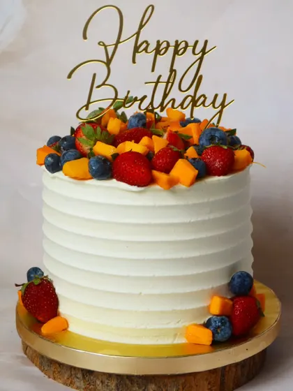Summer on a cake! A simple, elegant cake topped with a vibrant mix of fresh seasonal fruits like strawberries, blueberries, and mangoes.