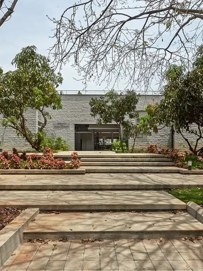 The entrance path to the KIPCER training center, winding through a grove of preserved trees. The journey into the building is as important as the building itself.