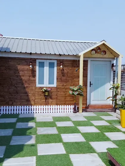 Our cottage-style prefab rooms add a touch of warmth and character. This unit features a wood-paneled exterior, a small porch, and decorative touches like a white picket fence.