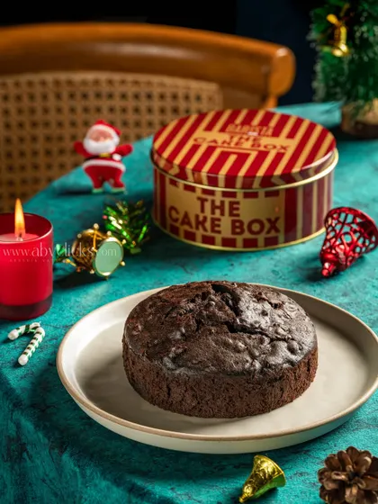 A classic Christmas fruit cake in a tin box, styled with a candle and ornaments to evoke a warm, festive feeling.