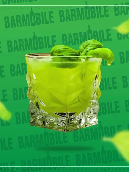 A vibrant green basil smash cocktail in a geometric glass. We use fresh herbs and ingredients to create bright, flavorful drinks.