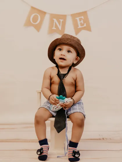 A stylish little man in a hat and tie poses for his first birthday studio session.