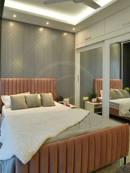 A photo of the finished bedroom, highlighting the custom pastel pink bed and the sleek sliding wardrobe with a full-length mirror. The result is a modern and glamorous space.