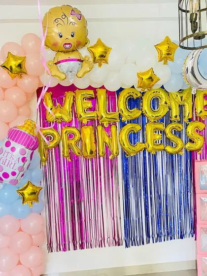 A "Welcome Princess" decoration for a baby girl. The setup includes a balloon arch, gold foil letter balloons, and "BABY" blocks.