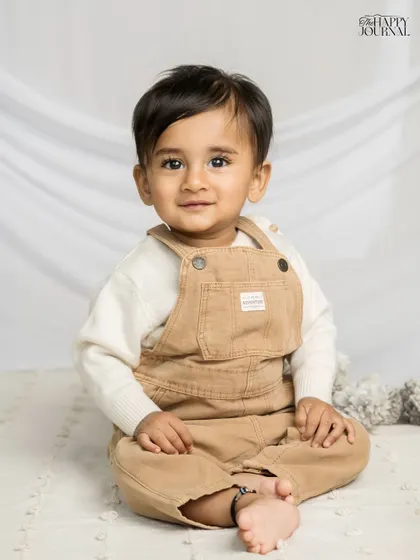 A baby boy in cute overalls gives a charming look to the camera. This simple studio portrait highlights his sweet expression and personality.