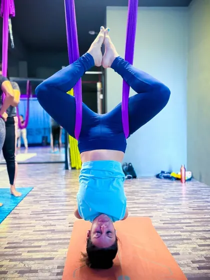 Here I am in an inverted butterfly pose, a core part of my aerial yoga flow. You can see another student in the background, showing the group setting where we all practice and support each other.